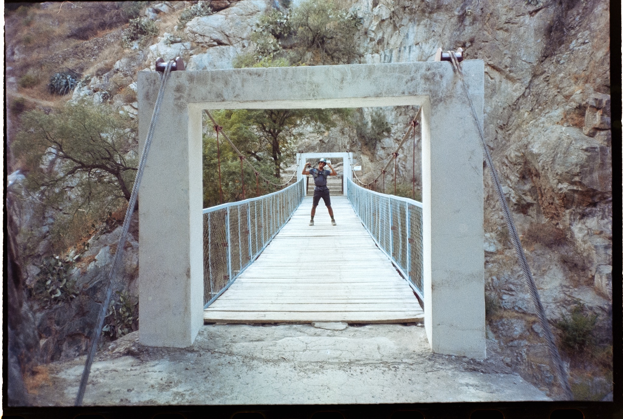 Oli auf einer Hängebrücke in einer felsigen Landschaft, auf analogem Film